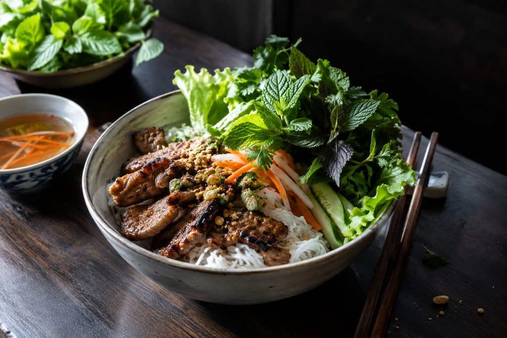 Bún mit gegrilltem Fleisch und frischen Kräutern auf dunklem Holz