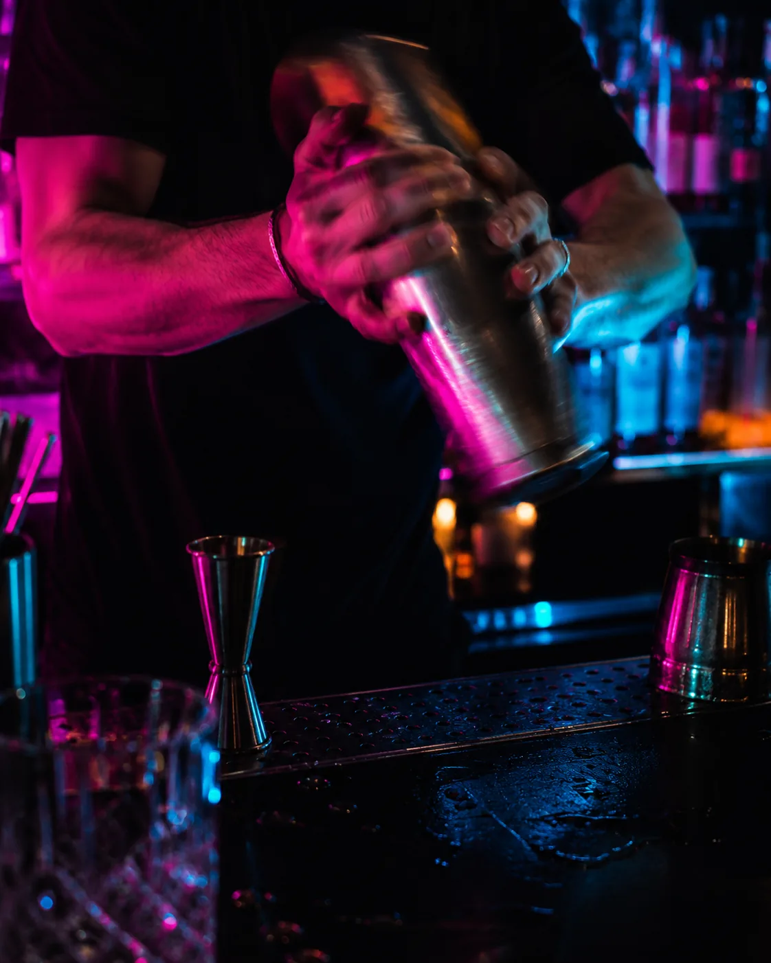 Bartresen bei Nacht in Neon-Pink und Cyan, Hände beim Mixen