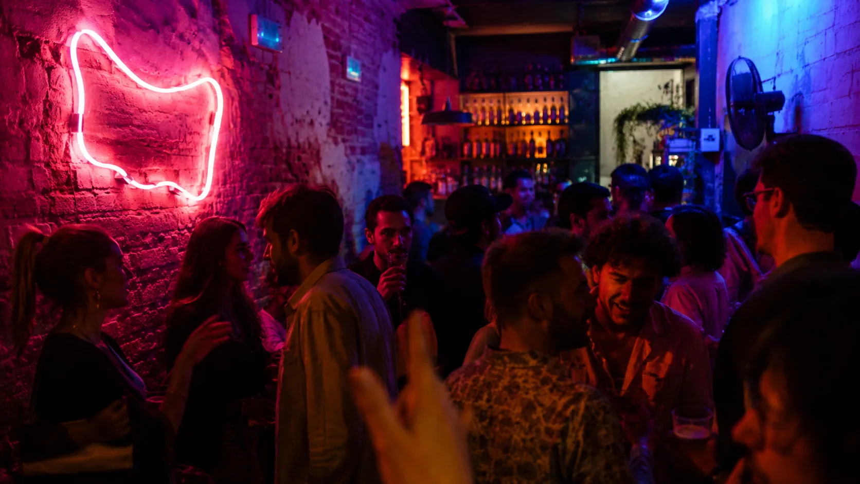 Voller Raum am Abend mit Neon-Schriftzug an der Wand und Menschen am Tresen
