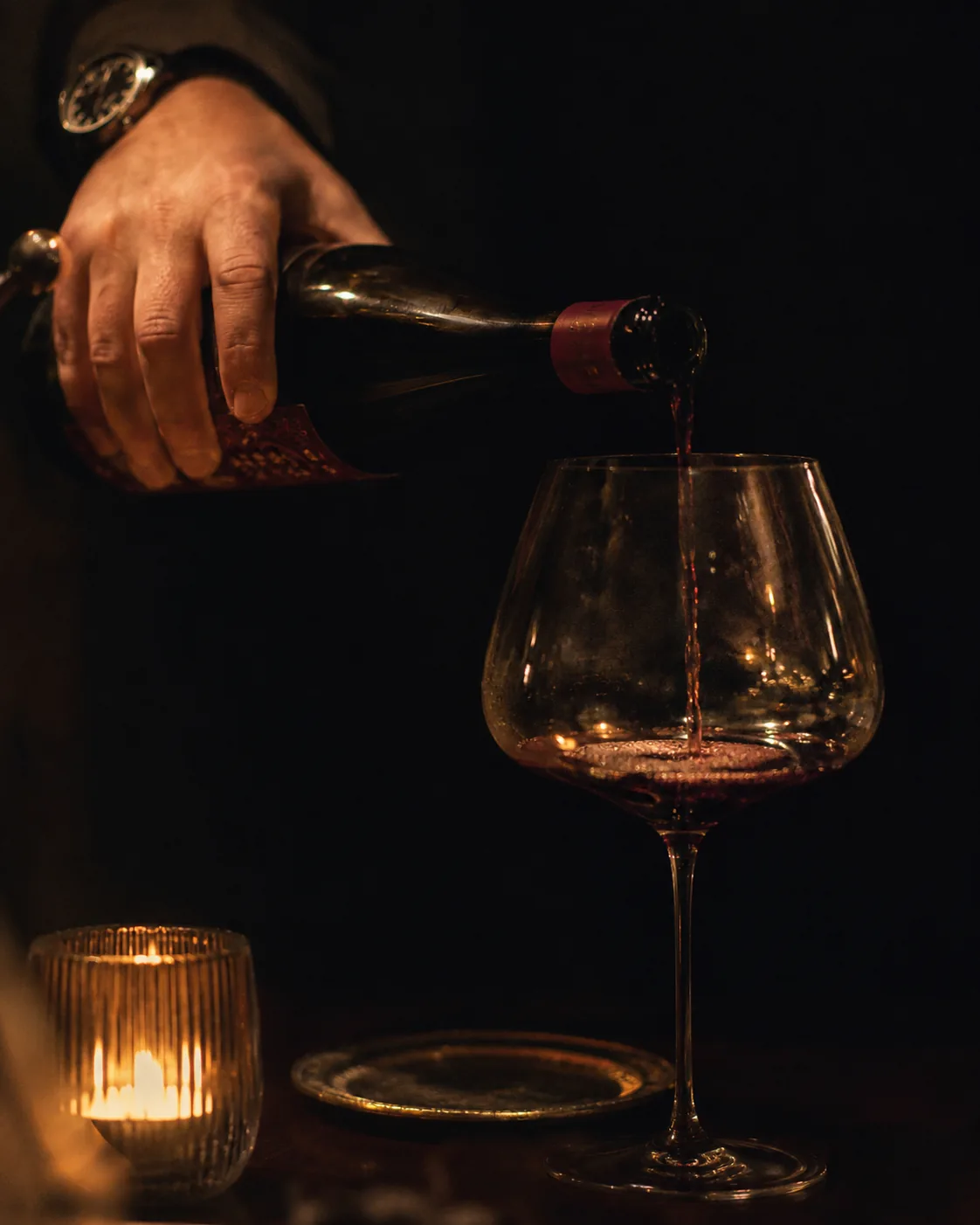 Hand schenkt Amarone bei Kerzenlicht ins Glas